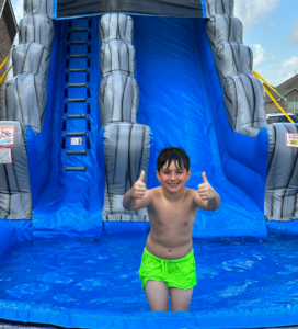 Child giving thumbs up in backyard inflatable water slide rental pool