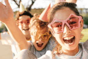 Kids wearing party hats and glasses smiling at a backyard celebration